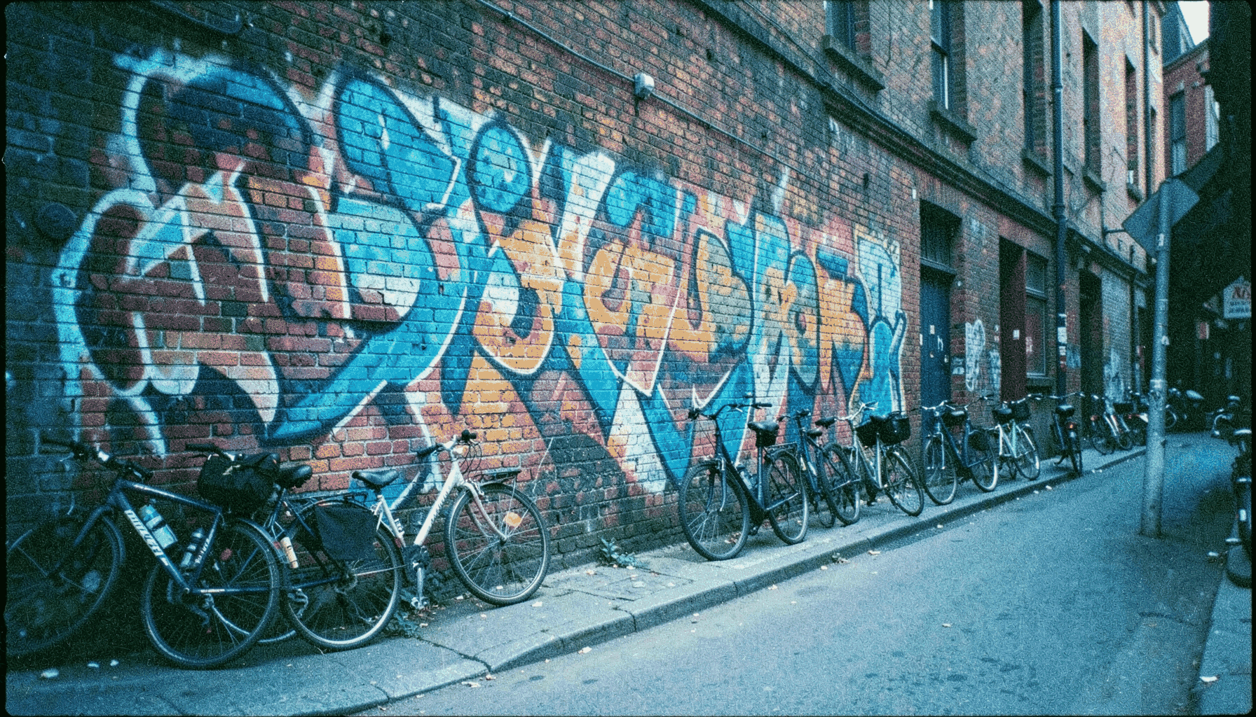 Mural de arte urbano en un muro de ladrillo visto con colores vibrantes, callejón con bicicletas aparcadas